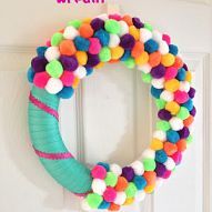 a colorful wreath with pom - poms and ribbon