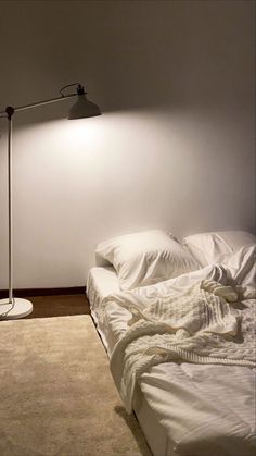 an unmade bed sitting next to a floor lamp