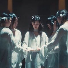 four young women in white robes standing together and looking at something on the screen behind them