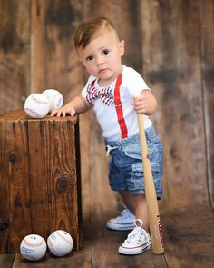 a young boy holding a baseball bat and standing next to a wooden box with balls on it