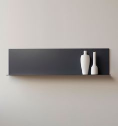 two white vases sitting on top of a black shelf next to a gray wall