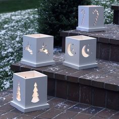 four white boxes with christmas decorations on them sitting on steps in front of snow covered bushes