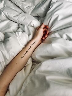 a person's arm with a tattoo on it laying under a white comforter