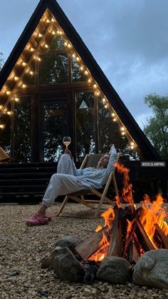 a person sitting in a chair next to a fire pit with lights on it and a building behind them