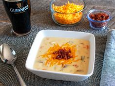 a bowl of soup with cheese and other condiments next to a glass of beer