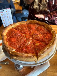 a deep dish pizza on a metal platter with people sitting at the table in the background