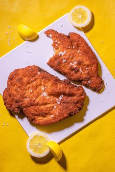 two pieces of fried chicken sitting on top of a cutting board next to lemons