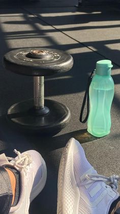 a person's feet next to a water bottle on the ground near a pair of shoes