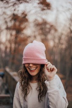 a woman wearing a pink hat and smiling at the camera with trees in the background