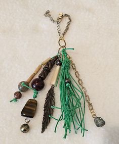 a green tasseled keychain with beads and feathers hanging from it's side