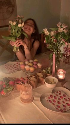 a woman sitting at a table with cupcakes and flowers