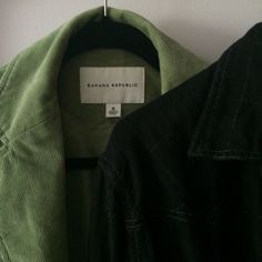 a green jacket hanging on a wall next to a black coat hanger with a white tag