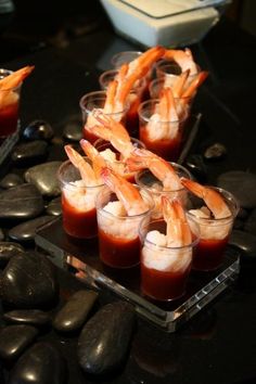 several small cups filled with shrimp on top of a black table next to some rocks