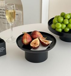 two black plates with green grapes and an apple on them next to a glass of wine