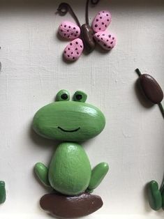 a green frog sitting on top of a white surface next to flowers and butterflies in the background