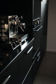 an espresso machine sitting on top of a black counter next to drawers and cabinets