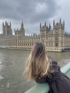 a woman looking out over the water in front of big ben and houses of parliament