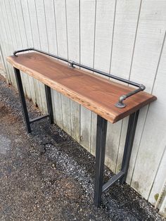 a long wooden bench sitting next to a white wall with black metal pipes on it