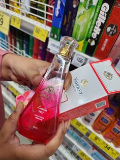 a person holding a bottle of perfume in front of a shelf with other products on it