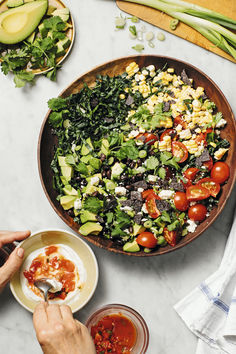 a person is cutting into a salad with tomatoes and avocado on the side