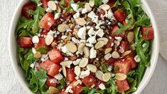 a salad with watermelon, feta cheese and almonds in a white bowl