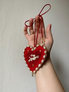 a woman's hand holding a red heart shaped ornament with an angel on it