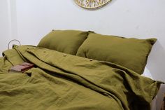 an unmade bed with green sheets and pillows on top of it, next to a clock