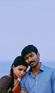 a man and woman standing next to each other in front of the ocean with their arms around each other