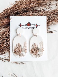 a pair of earrings with flowers and leaves on the front, sitting next to some dry grass