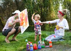 a man, woman and child are painting on the grass in front of some trees