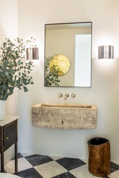 a bathroom sink sitting under a mirror next to a potted plant