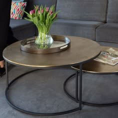 two tables with flowers on them sitting in front of a gray couch and coffee table