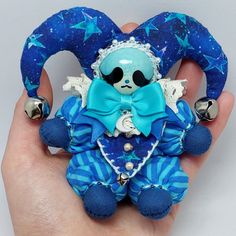 a hand holding a blue stuffed animal with stars on it's head and two bells in the shape of a heart