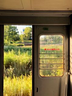 an open door leading to a grassy field and trees from inside a train car on the tracks