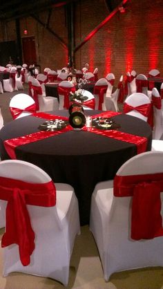 a banquet hall set up with white chairs and red sashes