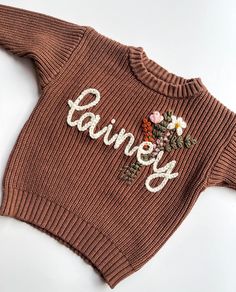 a brown sweater with flowers on it that says dainty written in white letters and the word dainty spelled out