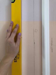 a hand holding a yellow ruler next to a wall