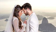 a bride and groom standing next to each other on top of a mountain overlooking the ocean