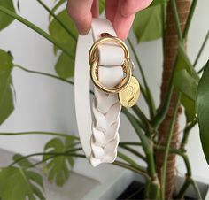 a person holding onto a white and gold ring with a coin on the end, in front of a potted plant