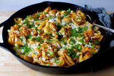 a skillet filled with pasta and vegetables on top of a wooden table next to a fork