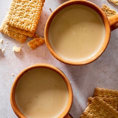 two mugs filled with milk and crackers on top of a white countertop