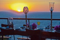 a table set up for dinner with the sun setting over the ocean in the background