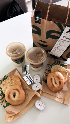 two bagels and coffee are sitting on the table next to some paper bags with donuts in them