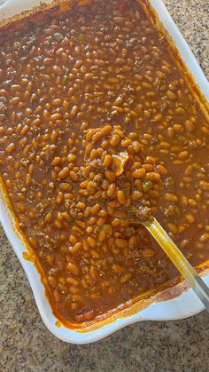 a spoon full of beans and meat in a dish on a counter top with a wooden spoon