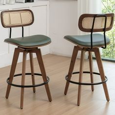 two wooden barstools with green leather seats in a white living room, next to a window