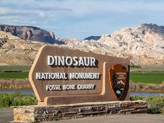 a sign for the dinosaur national monument in front of some mountains and grass, with a river running through it