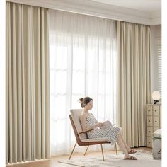 a woman sitting on a chair in front of a window with white drapes and curtains