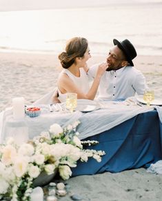 a man and woman sitting at a table on the beach