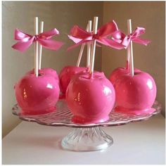 pink candy apples on a glass plate with sticks sticking out of the top and bowknots attached to them