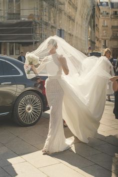 the bride is walking down the street with her veil blowing in front of her head